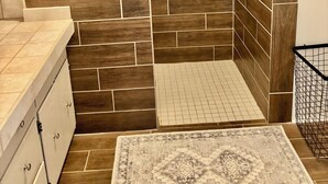 Un baño con zona de ducha, una ventana y un tapete estampado.
