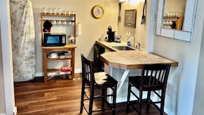 Una cocina compacta con una mesa de madera, dos sillas, un microondas, un lavamanos y un reloj.