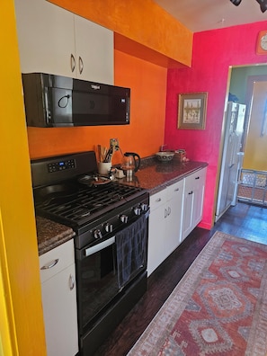 Una cocina con estufa, horno y microondas. Una pared es roja y hay una alfombra estampada.