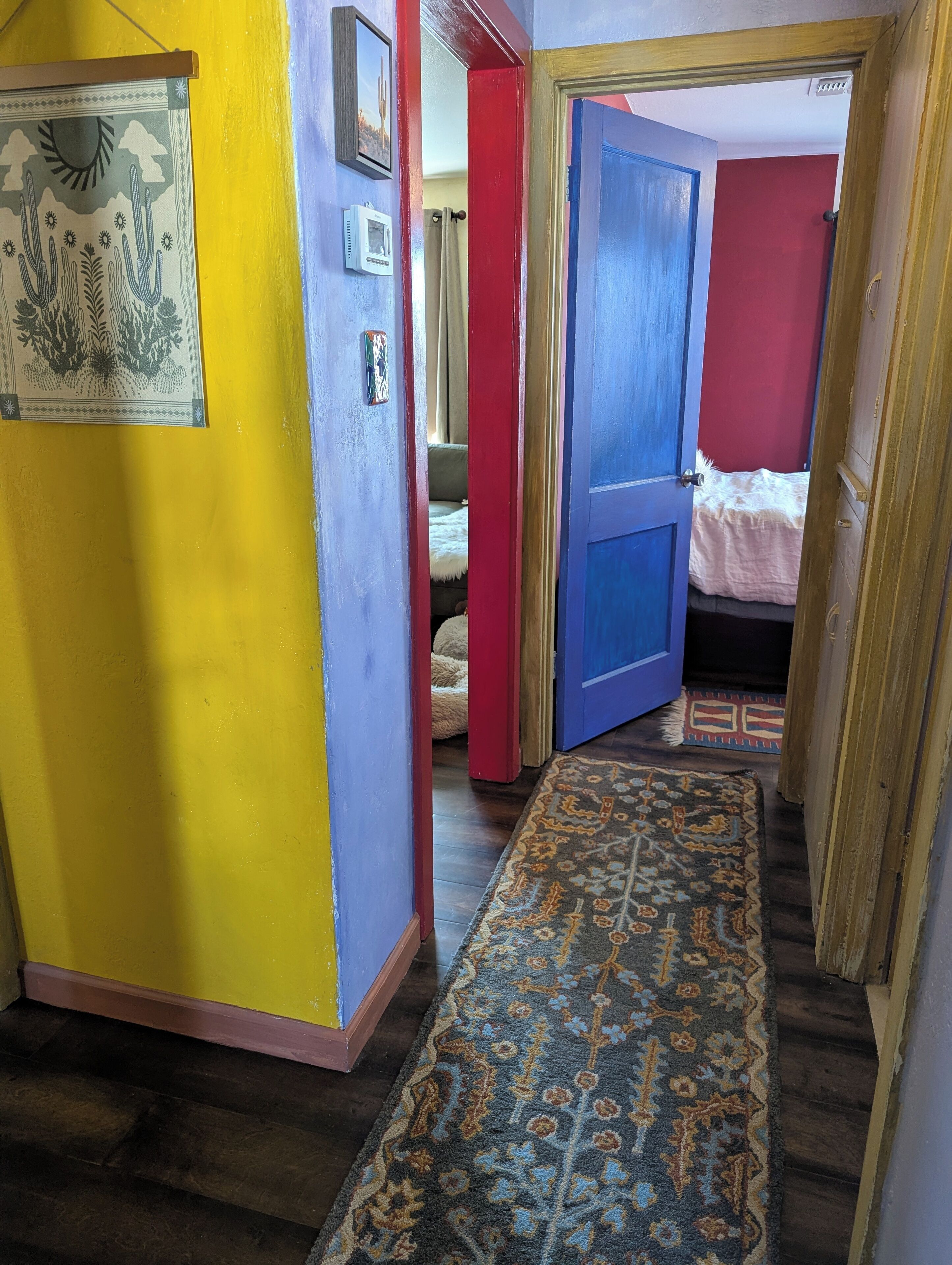 A hallway with a patterned rug, a bed with a red wall, and a door leading to another room.