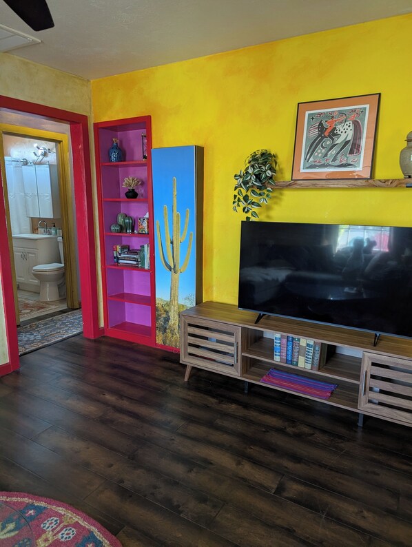 A living room with a TV, a bookshelf, a cactus decoration, and a bathroom visible through an open door.