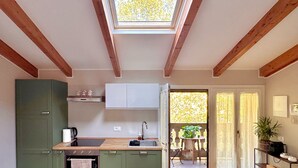 Ett modernt kök med träbjälkar, en matplats med en soffa och en utsikt genom en öppen dörr ut till en uteplats.