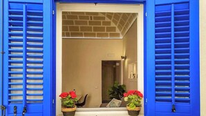 A doorway with blue shutters, two potted plants with red flowers, and a brick wall. - Il Rifugio (Marettimo)