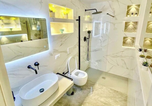 Un baño moderno con lavamanos, espejo y ducha blancos.