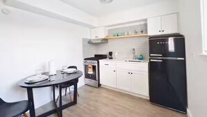 Une cuisine de taille réduite avec des meubles blancs, un réfrigérateur noir, une cuisinière et une table à manger avec des chaises.
