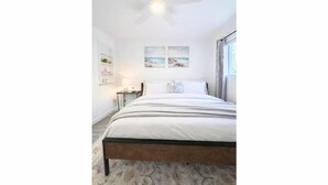 Une chambre à coucher comprenant un lit, un ventilateur de plafond, une table de chevet et deux tableaux accrochés au mur.