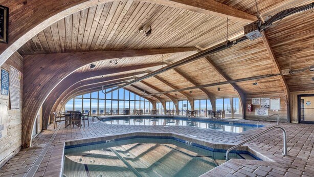 En indendørs swimmingpool med træbjælker og udsigt til havet.