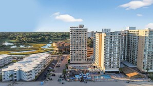 Et højt hotel med mange etager, et poolområde med liggestole og udsigt til et vandareal i nærheden.