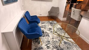 Un soggiorno moderno con una televisione a schermo piatto montata a parete, un divano blu, una poltrona grigia e un tavolino da caffè in vetro.