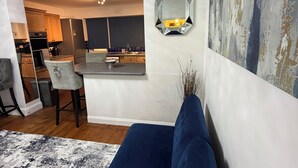 Un soggiorno moderno con un divano blu, una cucina sullo sfondo e uno specchio esagonale decorativo a parete.