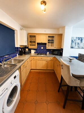 A compact kitchen with wooden cabinets, a built-in washing machine, and a bar stool.