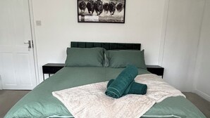 Una camera da letto con una coperta verde, una coperta bianca e un asciugamano arrotolato. Sulla parete, sopra il letto, c'è un quadro incorniciato.