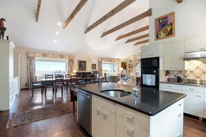A spacious kitchen with a central island, wooden beams on the ceiling, and a dining area with chairs and a table. - Oceanside Estate: Main House & Apt w/beach access (Gloucester)