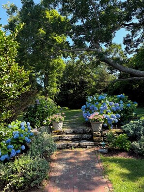 A garden pathway with a stone archway, surrounded by lush greenery and flowering plants. - Oceanside Estate: Main House & Apt w/beach access (Gloucester)