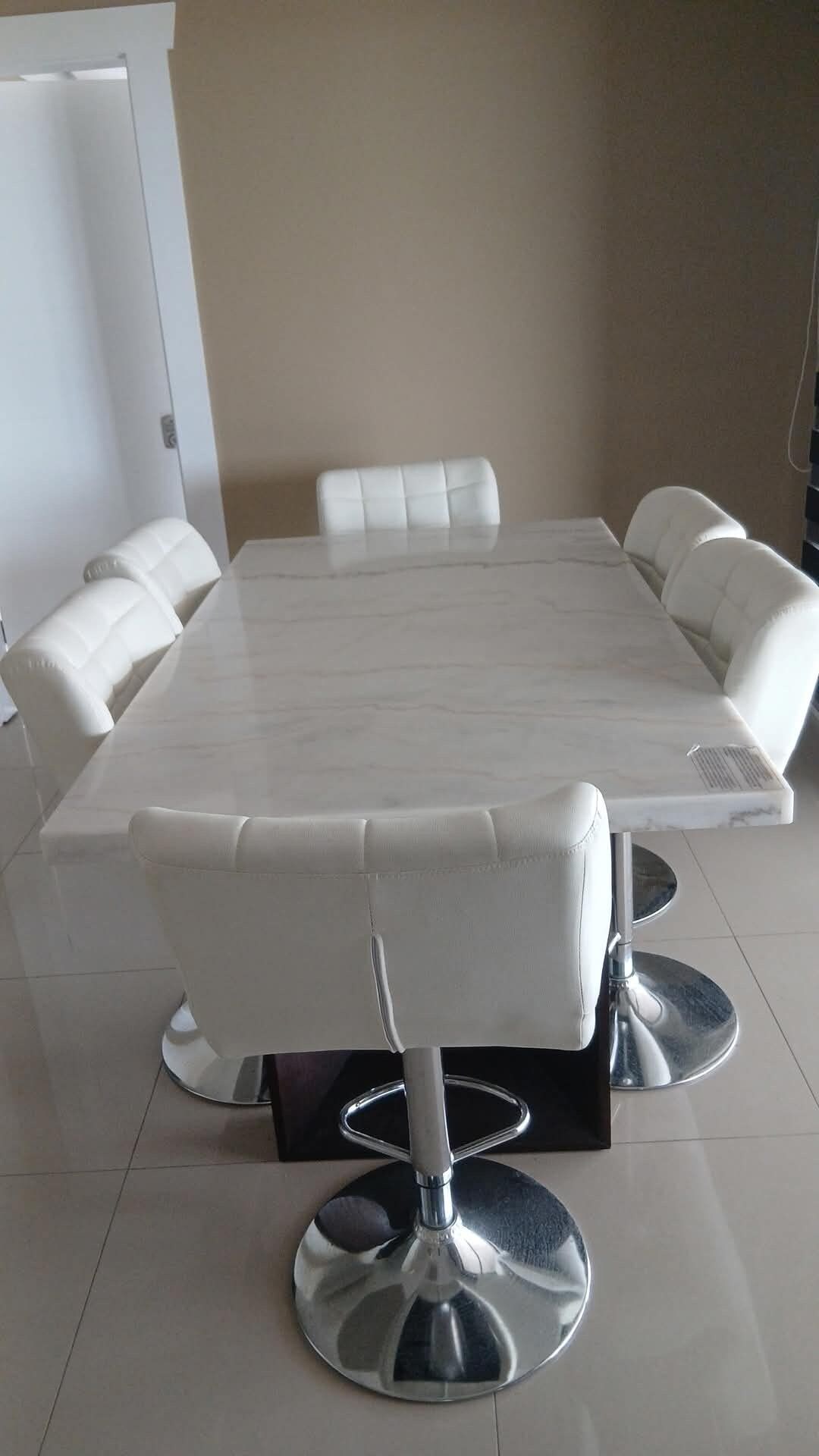 A rectangular dining table with a marble top, surrounded by six white cushioned chairs with metallic bases.