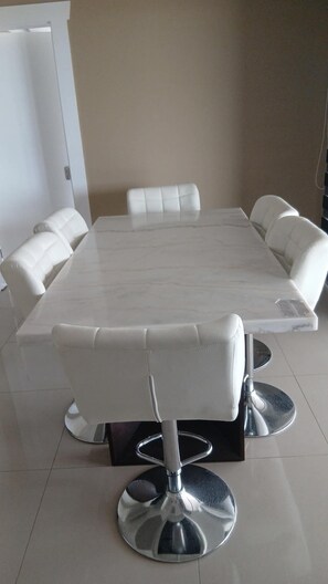 A rectangular dining table with a marble top, surrounded by six white cushioned chairs with metallic bases.