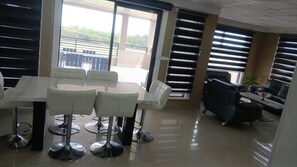 A modern interior with a dining area featuring a white table and four bar stools, a black office chair, and a sofa.