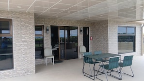 An outdoor patio with a table and chairs, a fire extinguisher, and a view through the glass doors.