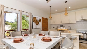 A modern dining area with a marble table, chairs, and a kitchen in the background. - Willow Estates Luxury Condo – Spacious 2BR 2BA Pool and Las Terrenas Beaches (Las Terranas)