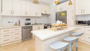 A modern kitchen with white cabinets, stainless steel appliances, and a marble island with bar stools. - Willow Estates Luxury Condo – Spacious 2BR 2BA Pool and Las Terrenas Beaches (Las Terranas)