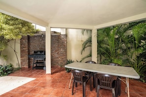Une terrasse extérieure avec un mur en briques, un barbecue et une table avec des chaises.