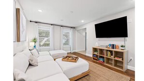 A modern living room with a sectional sofa, a flat-screen TV mounted on the wall, and a bookshelf filled with books and decorative items. - Winter snowbirds retreat- Monthly discount available for min 3 month stay (Gulf Breeze)