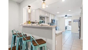 A kitchen with white cabinets, a microwave, and a ceiling fan. There are bar stools with wooden seats and turquoise metal frames. - Winter snowbirds retreat- Monthly discount available for min 3 month stay (Gulf Breeze)