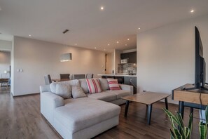 A modern living room with a sectional sofa, a dining table, and a kitchen area in the background.