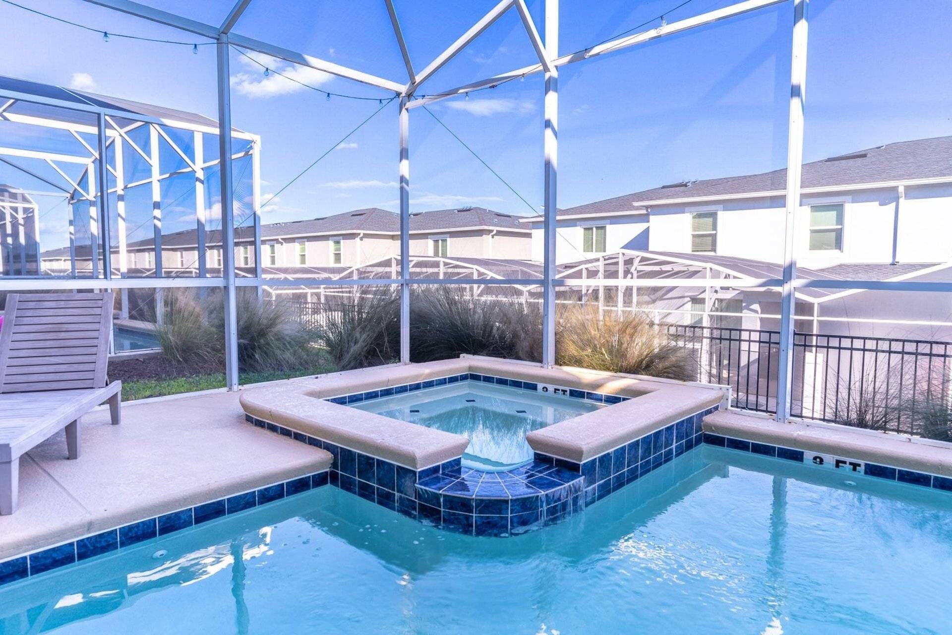 A swimming pool with a hot tub, surrounded by a covered area with a metal frame and glass panels.