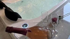 Une salle de bain moderne avec une grande baignoire, une coupe de champagne et un verre d’eau.