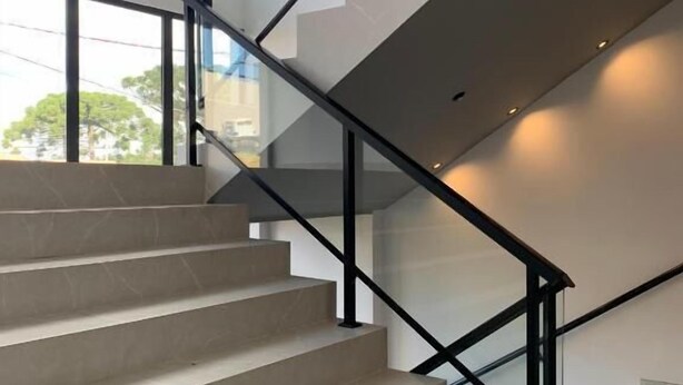 Un escalier moderne au design minimaliste, doté d’une rampe en verre et d’un motif géométrique sur les marches.