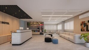 Un hall d’hôtel moderne comprenant un comptoir d’accueil, un espace salon et des distributeurs automatiques.