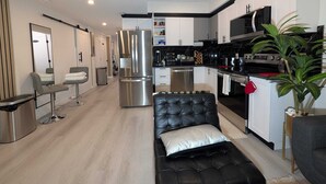 A modern kitchen with stainless steel appliances, a dining area with a black leather couch, and a small seating area with a mirror and chairs. - Serene 2-bedroom apartment in Calgary, perfect for your getaway- The Loft Modern (Calgary)