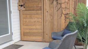 A covered patio area with two wicker lounge chairs, a wooden door, and a potted plant. - Serene 2-bedroom apartment in Calgary, perfect for your getaway- The Loft Modern (Calgary)