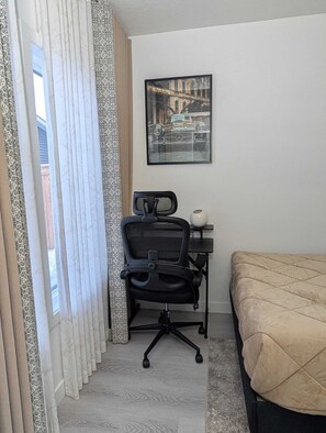Una habitación de hotel con una cama, un escritorio con una silla, un cuadro enmarcado en la pared y cortinas con estampado.