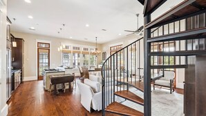 A spacious kitchen with wooden flooring, a dining area with white chairs, and a staircase leading to an upper level. - Community Pool Access with Carriage (Rosemary Beach)