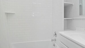 Ein modernes Badezimmer mit weißen, rechteckigen Fliesen, einer Badewanne, einer Dusche inklusive Duschbrause und einem Waschtisch mit Spiegel.
