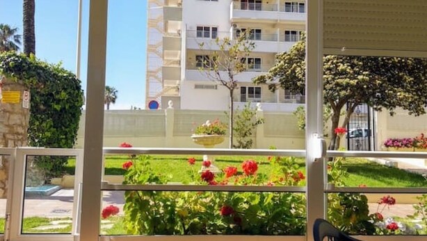 Een balkon met uitzicht op een gebouw, een tuin met rode bloemen en een stoel.