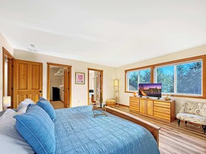 A bedroom with a large bed, wooden wardrobe, dresser, and a television on a wooden stand.