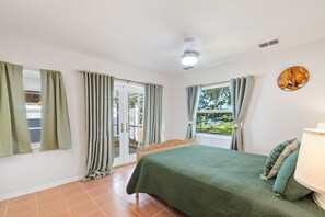 A bedroom with a bed, a window, and a door leading to an outdoor area. - Cedar Key Coastal Oak Retreat (Cedar Key)