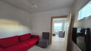 Una sala de estar con un sofá rojo, un sillón gris, un pequeño otomaní y un televisor de pantalla plana montado en la pared.