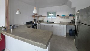 Una cocina con isla central, vigas de madera, lámparas colgantes, un ventanal y un refrigerador.