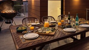 Un área de comedor al aire libre con una mesa dispuesta para una comida, una parrilla y vistas al atardecer.