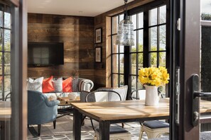 A cozy living room with a wooden wall, a flat-screen TV, a sofa with patterned cushions, and a dining table with a vase of flowers. - Panoramic sea views, private terrace, parking, jacuzzi, pool, gym (Falmouth)