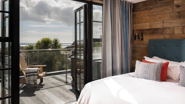 A bedroom with a large window, a view of the outdoors, a wooden headboard, and a bed with patterned pillows. - Panoramic sea views, private terrace, parking, jacuzzi, pool, gym (Falmouth)