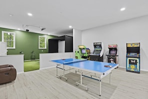 A room with a ping pong table, arcade games, and a green wall.