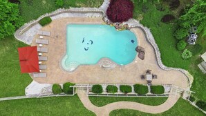 An aerial view of a swimming pool with a red umbrella, lounge chairs, and surrounding greenery. - 8,000 Sq Ft Luxury Estate Near Annapolis | Sleeps 32 | Pool, Theater & Pickleball (Davidsonville)