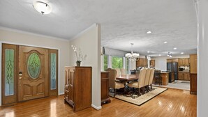 A spacious dining area with a wooden table and chairs, a chandelier, and a view of the kitchen. - 8,000 Sq Ft Luxury Estate Near Annapolis | Sleeps 32 | Pool, Theater & Pickleball (Davidsonville)