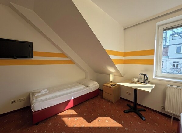 A small, compact room with a bed, a desk, a chair, a lamp, and a window. - Hotel Alser (Vienna)