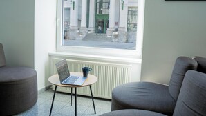 Una habitación con vista a un edificio que dice 'ALSER STRASSE', una mesita con una laptop y una taza, y dos sillones grises.